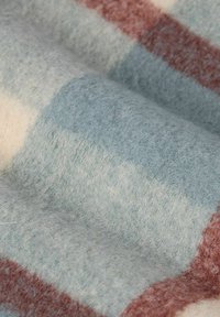 Couverture en laine avec un motif à carreaux bleu, crème et rouille, texture douce, surface pelucheuse et sections de design à carreaux bien marquées.