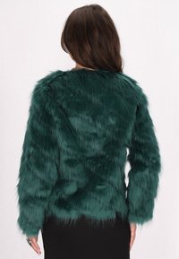 Giacca in pelliccia sintetica verde con maniche lunghe, finitura testurizzata e design corto, vista da dietro su uno sfondo bianco neutro.