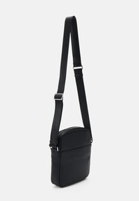 Borsa a tracolla nera in materiale testurizzato, con forma rettangolare, tracolla regolabile e apertura con zip, dotata di una tasca frontale.