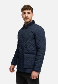 Chaqueta acolchada de color navy con patrón de diamante, botones de presión, bolsillos delanteros y cuello de pana. Fabricada con tejido texturizado y resistente al agua.