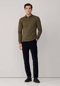 Zelené olivovo zelené polo tričko s dlhými rukávmi a golierom, kombinované s námorníckymi modrými nohavicami, s úzkym strihom a hladkou textúrou látky.