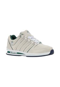 Scarpa sportiva beige chiaro con dettagli verdi, texture in suede, lacci bianchi e suola imbottita. Presenta un logo sul lato.