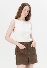 Top bianco a coste senza maniche abbinato a una mini gonna in corduroy marrone con grandi tasche e chiusura frontale a bottoni.