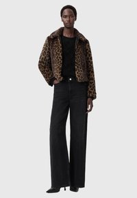 Lauva raksta mākslīgā kažokā ar plašu apkakli, apvienota ar melnu teksturētu džemperi un augsto vidukļa melnu platā stila biksēm.