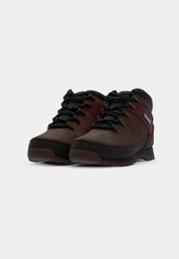 Brown suede hiking boots with black accents, featuring black laces, a rounded toe, a textured sole, and a small logo on the side.