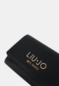Portafoglio in pelle nera con texture, caratterizzato da un logo dorato "LIU·JO MILANO". Design compatto con chiusura a patta e angoli arrotondati.