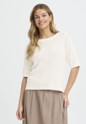 Kreemikas lühikeste varrukatega kudumist kampsun, vertikaalse soonilise tekstuuriga; lõdvestunud lõige ja lai kaelus. Kandmis all voolava pruuni seelikuga.