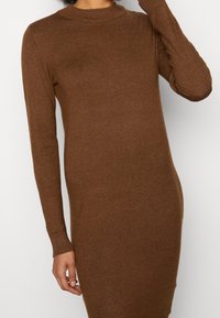 Abito lungo marrone a maniche lunghe in un morbido tessuto a maglia con scollatura rotonda e polsini a costine, progettato per una silhouette aderente.