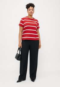 Κόκκινη ριγέ κοντομάνικη μπλούζα με λευκές οριζόντιες ρίγες, συνδυασμένη με μαύρο παντελόνι φαρδύ και μικρή μαύρη τσάντα.