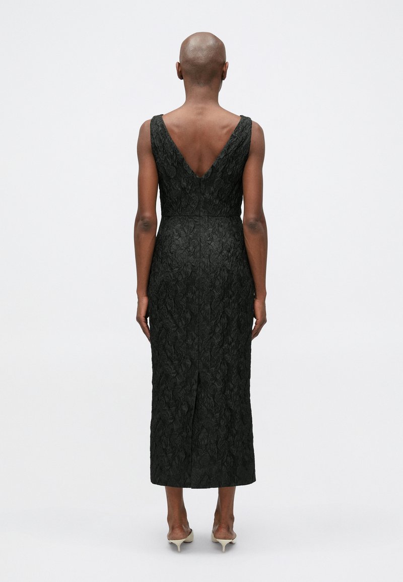 Black dress with a textured floral pattern, V-back design, fitted waist, and midi length, featuring a back slit and sleeveless style.
