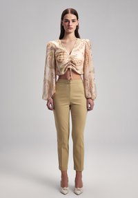 Blumenbedruckte Cropped-Bluse mit Puffärmeln, Kordelzugdetails und beigen, figurbetonten Hosen, kombiniert mit beigen Schuhen mit Knotenverzierung.
