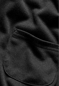 Tissu noir avec une texture lisse, comprenant une seule poche cousue. Le matériau est doux et légèrement extensible, idéal pour une tenue décontractée.