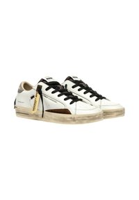 Sneaker bianco in pelle con lacci neri, dettagli in camoscio e tacco beige. Presenta etichette con logo e una suola in gomma testurizzata con una finitura sbiadita.