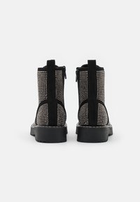Black ankle boots with a studded design, suede material, rear zippers, and a chunky sole, showcasing an alternating textured pattern.