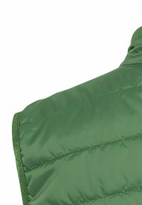 Gilet isolant vert avec une texture lisse et brillante, un motif matelassé et un bord vert contrastant le long des bords.