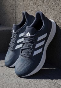 Baskets de sport navy avec trois rayures blanches, dessus en synthétique, design texturé et semelle en caoutchouc, avec fermeture à lacets et col rembourré.