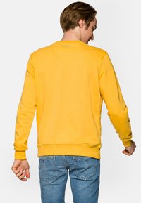 Żółta bluza z okrągłym dekoltem, długim rękawem, wykonana z miękkiego materiału, z prążkowanymi mankietami i dołem, gładki design bez wzorów czy grafik.