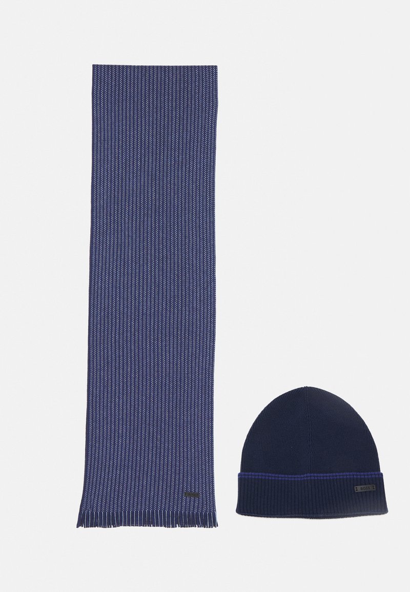 Sciarpa lavorata a maglia blu navy con texture a coste e estremità frangiate, abbinata a un berretto a coste con una striscia viola a contrasto.