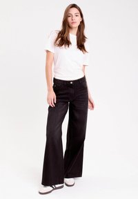 Bredde sorte denim jeans med høj talje, udstyret med knaplukning og klassisk fem-lomme design. Parret med en hvid t-shirt og sneakers.