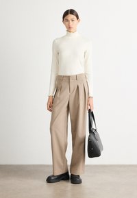 Cremefarvet turtleneck-top med flæsekrave, beige high-waisted plisserede bukser, sort håndtaske og kraftige sorte platform-sko.