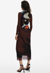 Rochie bodycon cu mânecă lungă, având o baza maro și modele abstracte în nuanțe de albastru, verde și roșu. Partea inferioară este transparentă, fiind asortată cu sandale cu toc negre.