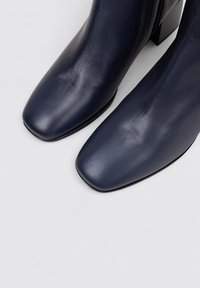 Botas de tobillo de cuero azul marino con punta cuadrada, textura suave y tacón bloque, con un cierre de cremallera lateral para facilitar el uso.