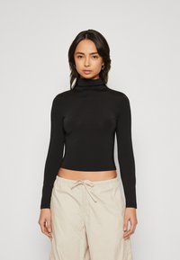 Svart langermet turtleneck-genser laget av glatt, elastisk stoff, med en tettsittende design og en cropped hem, kombinert med beige shorts med snøring.