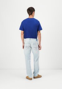 Camiseta de algodón azul combinada con jeans de denim azul claro. Los jeans cuentan con sutiles bolsillos traseros bordados y un corte relajado. Calzado marrón completa el conjunto.