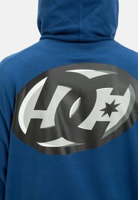 Blue hoodie with a large black and silver graphic logo on the back. Cotton material, soft texture, and a relaxed fit with a hood.