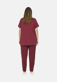 Bordeaux kleurig bijpassend set bestaande uit een losse, korting mouw blouse en taps toelopende broek, gemaakt van zachte stof met een gladde textuur.