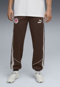 Brune sportbukser med hvide accenter, der har sidelængder med et geometrisk mønster, logo-patch og en afslappet pasform.