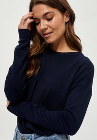 Pull bleu marine en tissu doux, avec un col rond, des manches longues et des poignets côtelés. Design minimaliste, coupe décontractée.