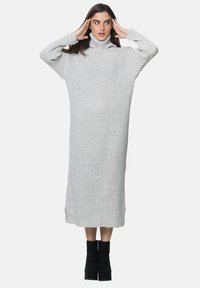 Hellgraues, geripptes Strickkleid mit Rollkragen, langen Ärmeln, mittellang bis zur Wade und seitlichen Schlitzen. Kombiniert mit schwarzen Stiefeletten.