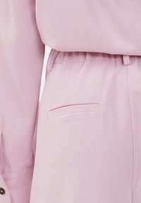 Ροζ λινό σύνολο που περιλαμβάνει ένα χαλαρό μπλουζάκι και παντελόνι δέσιμο στη μέση με πλαινές τσέπες, δείχνοντας ομαλή υφή και ελάχιστες λεπτομέρειες ραψίματος.