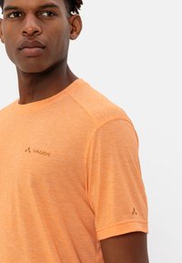 T-shirt sportivo a maniche corte, di colore arancione, con una texture melangiata. Presenta un logo VAUDE discreto sul petto e un piccolo accento del logo sulla manica.