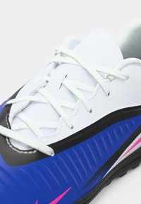 Αθλητικά παπούτσια με λευκό συνθετικό πάνω μέρος, μαύρες και μπλε υφασμάτινες λεπτομέρειες από αφρό, ροζ λογότυπο και λευκές κορδόνες.