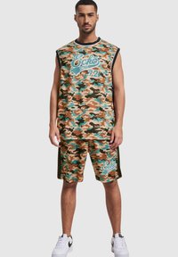 Kamuflasje uten ermer topp og shorts i brun, grønn og blå med "Ecko Unltd 72" grafikk. Laget av lett materiale. Hvite joggesko.
