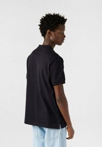 Polo nero con colletto classico, maniche corte e orlo dritto. Il tessuto appare liscio con una vestibilità rilassata e un design minimale.