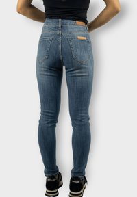 Jeans ajustados en denim azul claro con cintura alta, con dos bolsillos traseros y acentos de cuero marrón cerca de la cinturilla.