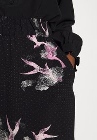 Tessuto nero con un motivo di uccelli rosa e pois bianchi. Presenta una vita elastica e dettagli di maniche arricciate. Texture morbida.
