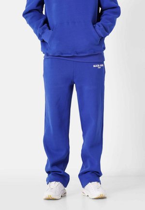 Pantalones de chándal azules con un ajuste relajado, hechos de una tela suave; presentan un pequeño logo blanco en la parte delantera y puños acanalados.