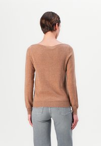 Brązowy sweter dzianinowy z szerokim dekoltem, długimi rękawami i prążkowanym dołem, w zestawieniu z szarymi dżinsami. Miękka tekstura, prosty fason i neutralne kolory.