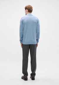 Ανοιχτό μπλε πλεκτό μπουφάν με ριχτό τελείωμα και μανσέτες, φορεμένο με σκούρα γκρι κοστούμια παντελόνια και μαύρα παπούτσια, βλέπεται από πίσω.