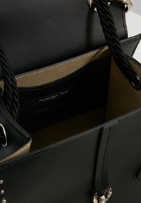 Mustat nahkakahvat, joissa on sileä pinta, köysisangat, kultainen vuorikangas ja hopeiset yksityiskohdat. Sisäpuolen etiketti näkyvissä.