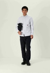 White and navy striped button-up shirt, dark pants, and black shoes. Carrying a small black bag with a textured finish.