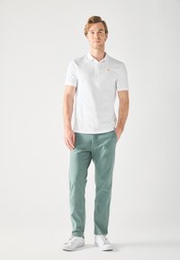 White polo shirt with short sleeves, featuring a small yellow logo; paired with light green pants and white sneakers. Simple design and fit.