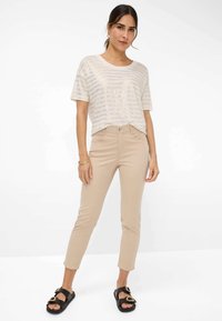 Beige gestreepte T-shirt met een ontspannen pasvorm, gecombineerd met tapered beige broek en zwarte slippers met gouden hartaccenten.