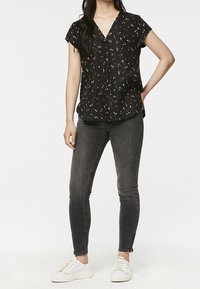 Blouse noire à manches courtes en V avec un motif abstrait coloré, associée à un jean gris skinny et des baskets blanches.