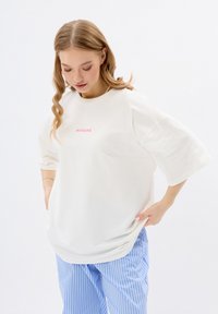 T-shirt blanc ample à manches courtes et col rond. Caractérisé par le texte rose "MIRONS" centré sur la poitrine. Matière en coton doux.