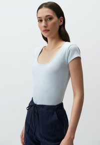 Jasnoniebieski, prążkowany bodysuit z dekoltem w serek i krótkimi rękawami, w połączeniu z granatowymi spodniami na sznurku. Gładka tekstura i dopasowany krój.